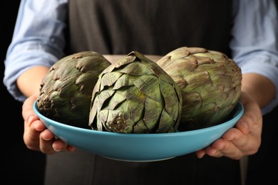 Photo of Woman holding bowl with fresh raw artichokes, closeup