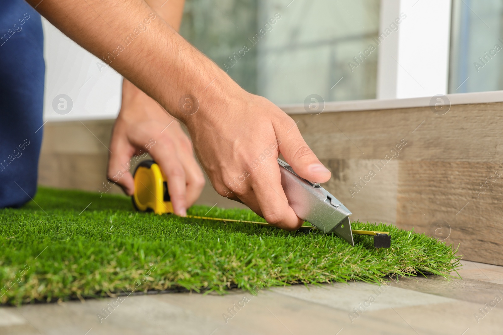 Photo of Man cutting artificial grass carpet indoors, closeup