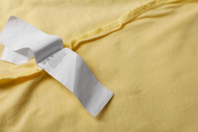 Photo of Clothing label on beautiful yellow garment, closeup. Space for text