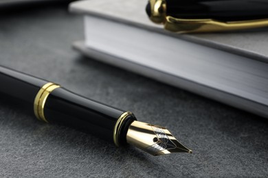 Photo of Stylish black fountain pen and notebook on grey textured table, closeup