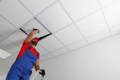 Photo of Electrician repairing ceiling light indoors, low angle view. Space for text