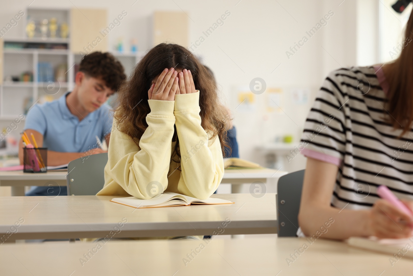 Photo of Teen problems. Lonely girl sitting separately from other students in classroom