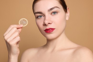 Photo of Woman holding condom on beige background. Safe sex