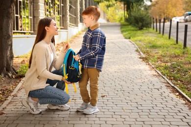 Young mom giving school backpack to her son outdoors