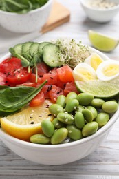 Delicious poke bowl with quail eggs, fish and edamame beans on white wooden table, closeup