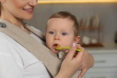 Photo of Mother feeding her cute child in sling (baby carrier) indoors