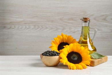 Photo of Sunflower cooking oil, seeds and yellow flowers on white wooden table, space for text