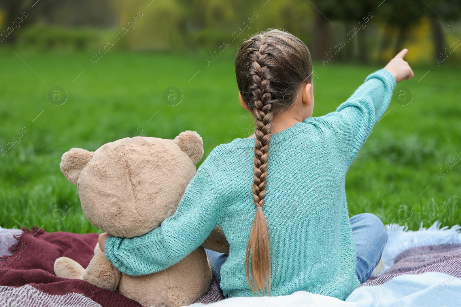 Photo of Little girl with teddy bear on plaid outdoors, back view