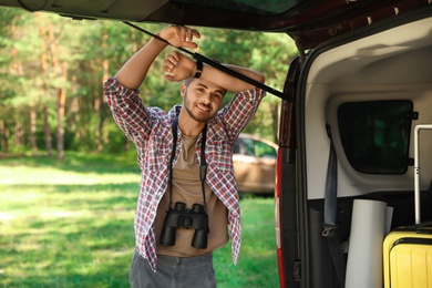 Photo of Young man with binoculars near van in forest. Camping gear