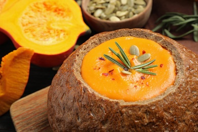 Tasty pumpkin cream soup in bread loaf on wooden board, closeup