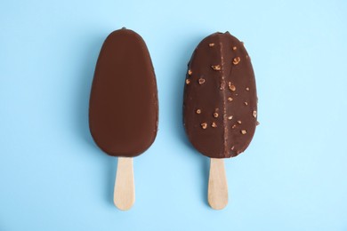 Photo of Ice cream bars glazed in chocolate on light blue background, flat lay