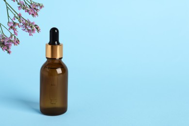 Photo of Bottle with cosmetic oil on podium and flowers on light blue background, space for text