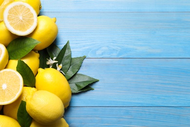 Many fresh ripe lemons with green leaves and flowers on blue wooden table, flat lay. Space for text