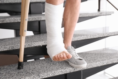 Photo of Young man with crutch and broken leg in cast on stairs