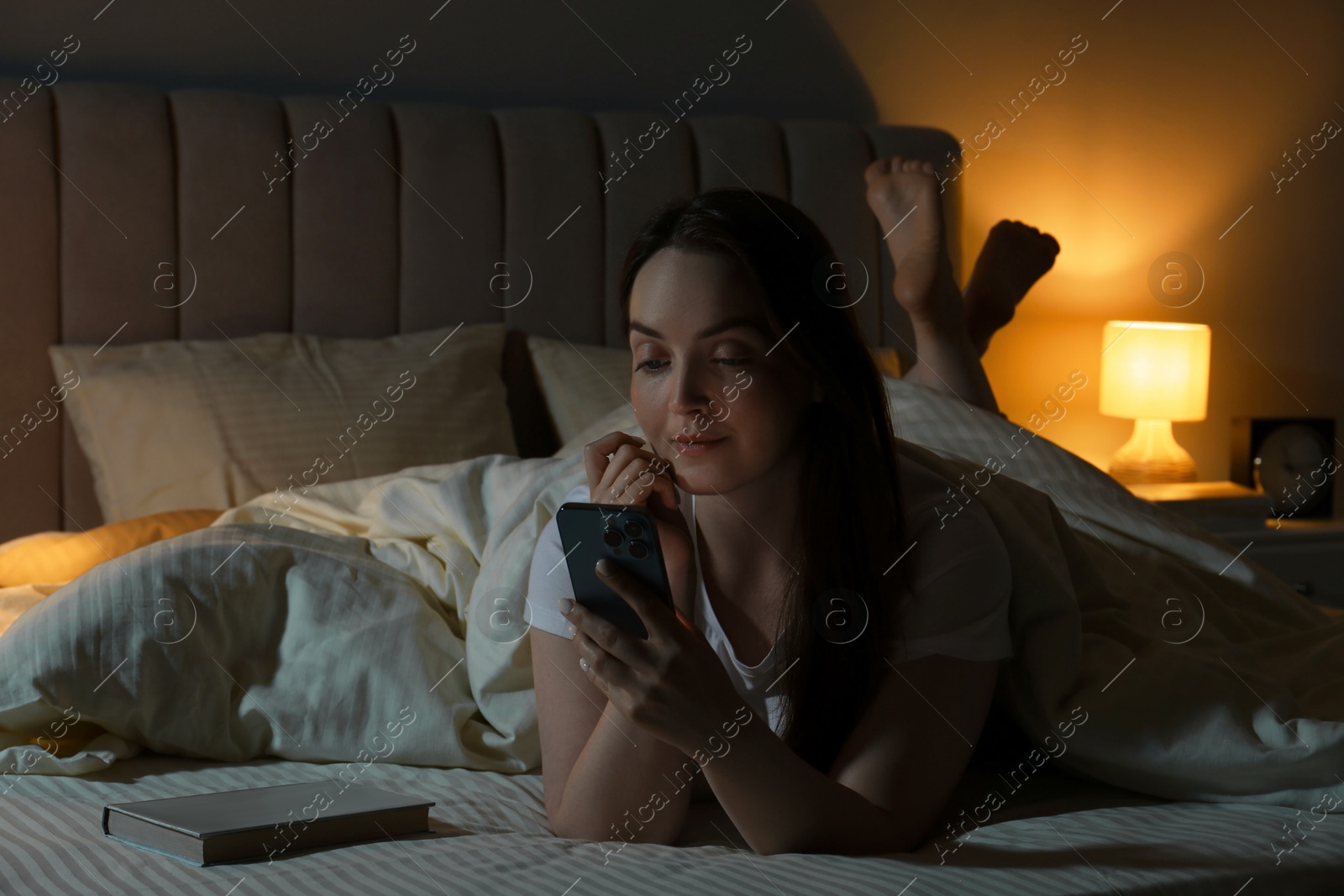 Photo of Woman using smartphone in bed at night. Internet addiction