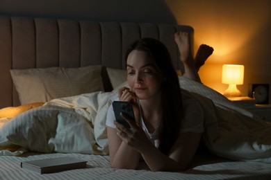 Photo of Woman using smartphone in bed at night. Internet addiction