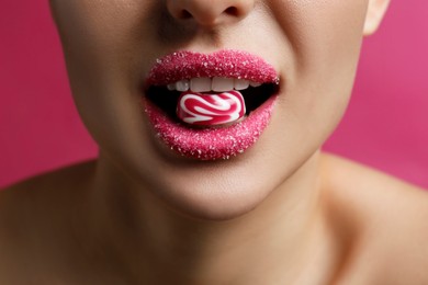 Woman with lips covered in sugar eating candy on pink background, closeup