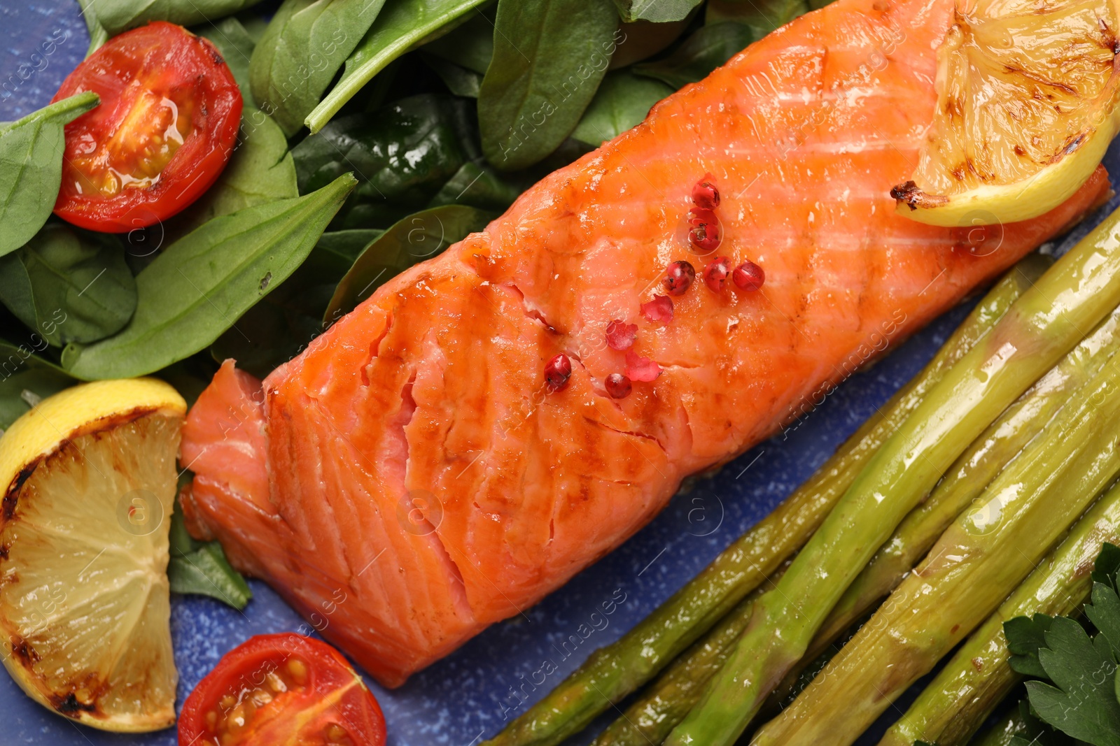 Photo of Tasty grilled salmon with tomatoes, asparagus, lemon and basil on plate, top view