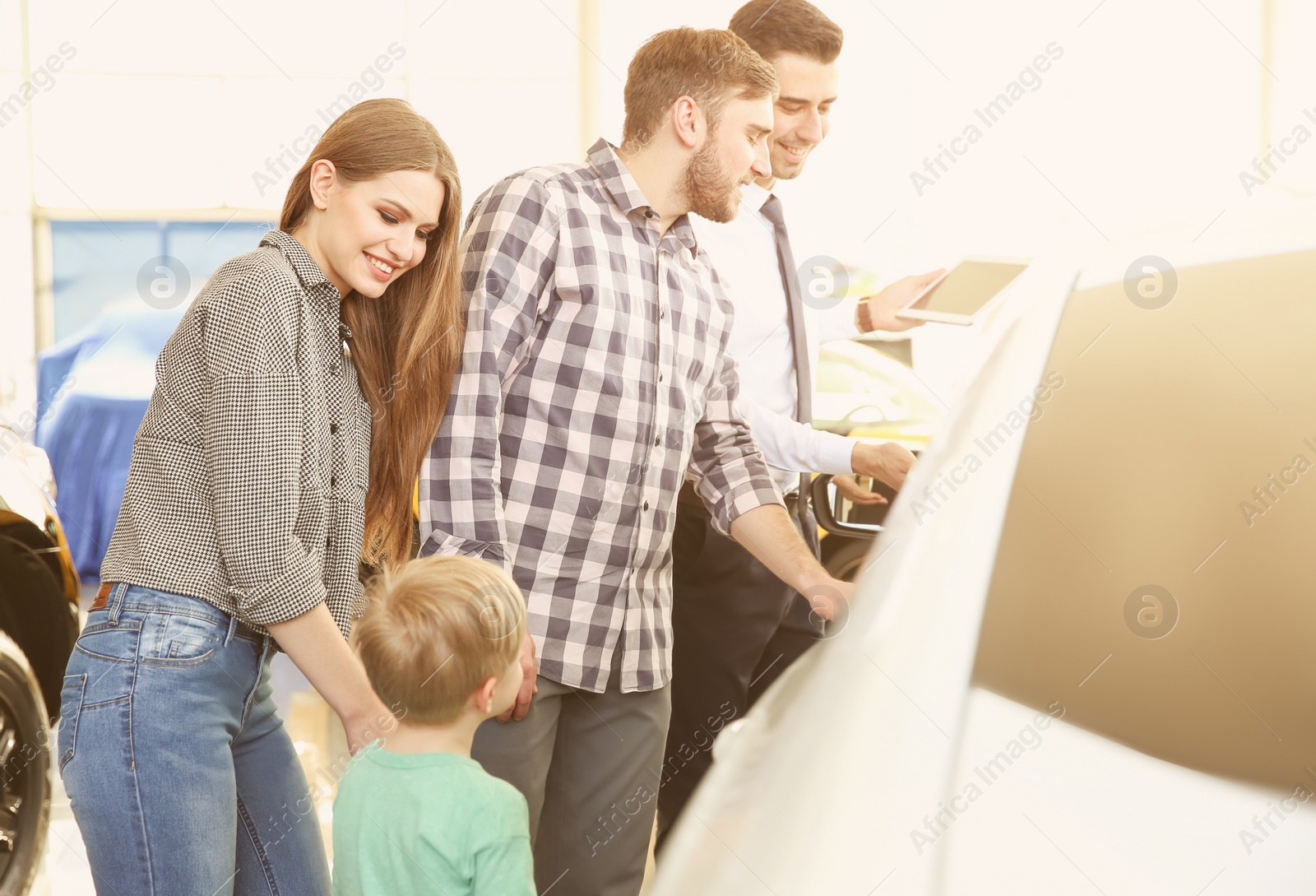 Photo of Young family choosing new car with salesman in salon