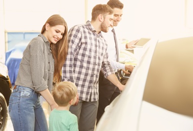 Photo of Young family choosing new car with salesman in salon