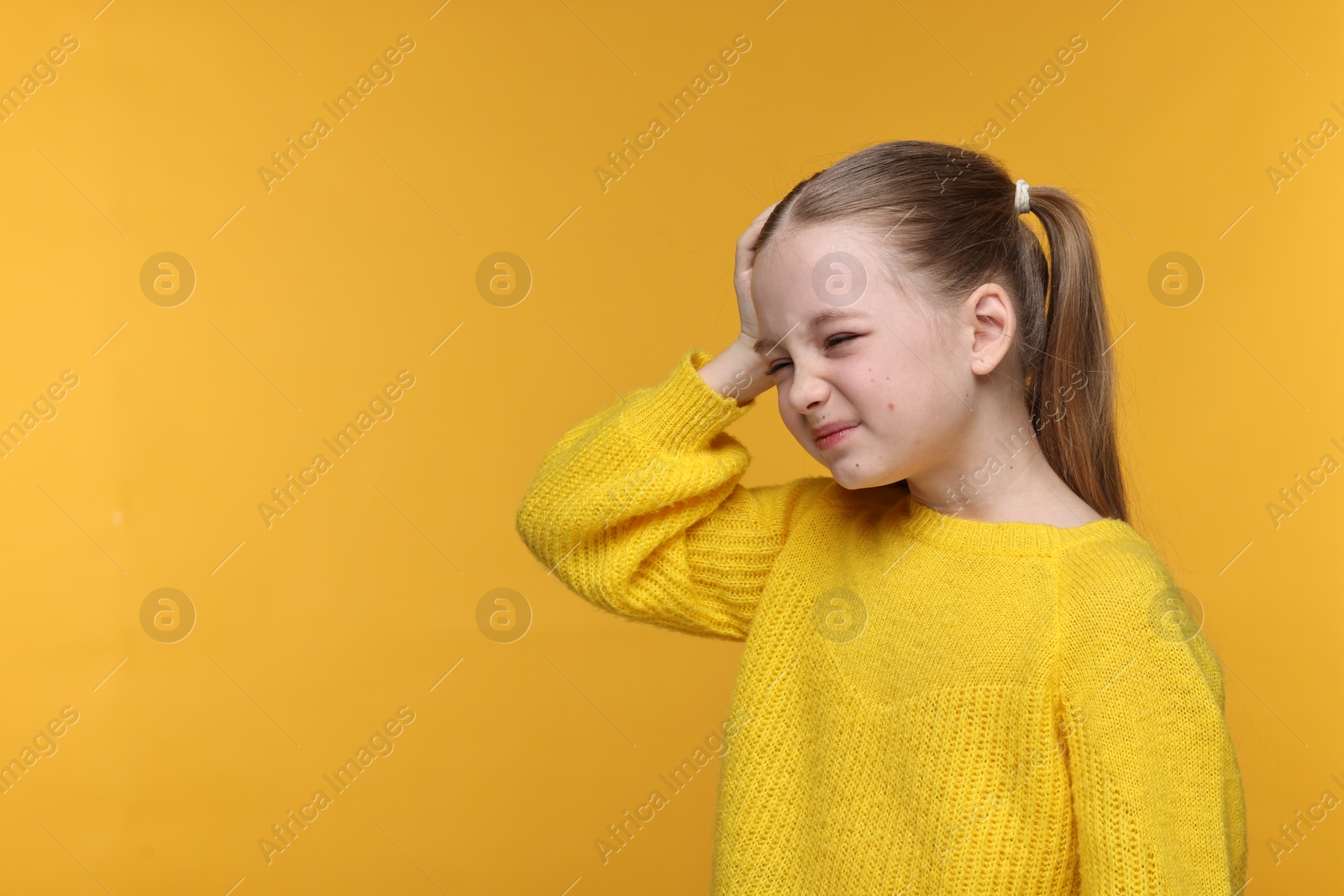 Photo of Little girl suffering from headache on yellow background. Space for text
