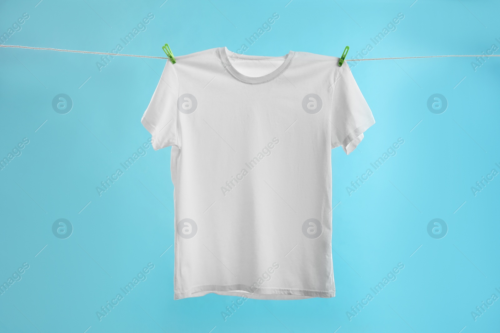 Photo of One white t-shirt drying on washing line against light blue background