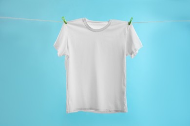 Photo of One white t-shirt drying on washing line against light blue background