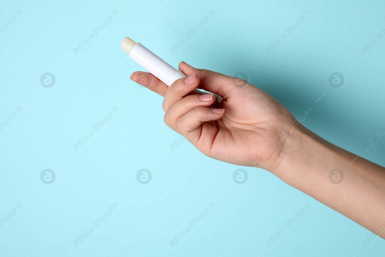 Photo of Woman holding hygienic lipstick on turquoise background, closeup