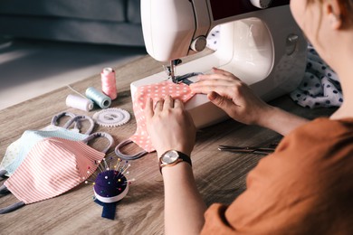 Photo of Woman sewing cloth protective mask with machine at table indoors, closeup