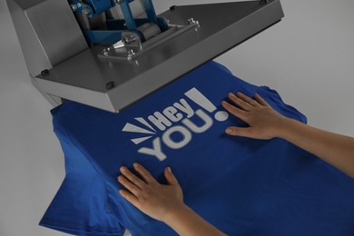 Photo of Printing logo. Woman with t-shirt using heat press at white table, closeup
