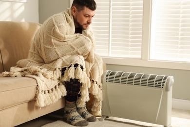 Man warming hands near electric heater at home