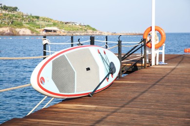 Photo of SUP board with paddle on wooden pier near sea