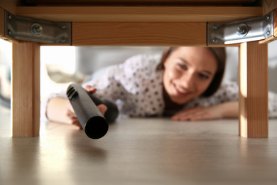 Photo of Young woman using vacuum cleaner at home