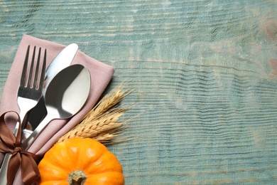 Photo of Top view of cutlery with napkin, wheat spikes and pumpkin on blue wooden table, space for text. Thanksgiving Day