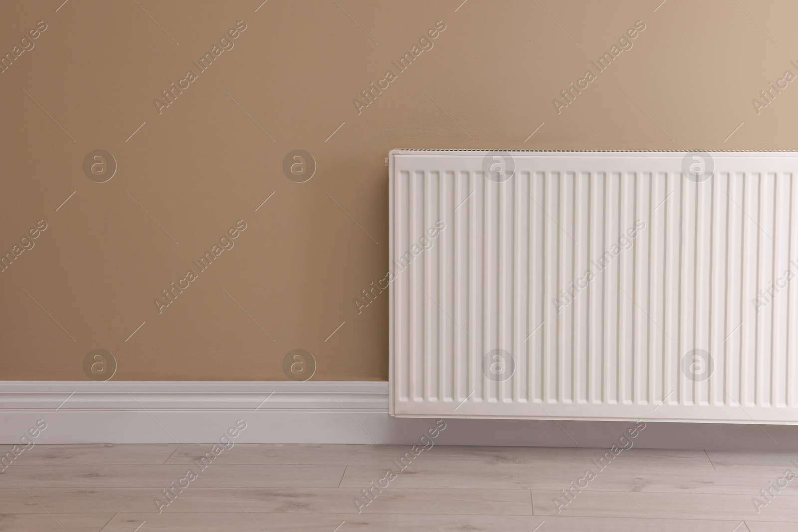 Photo of Modern radiator on beige wall, space for text. Central heating system
