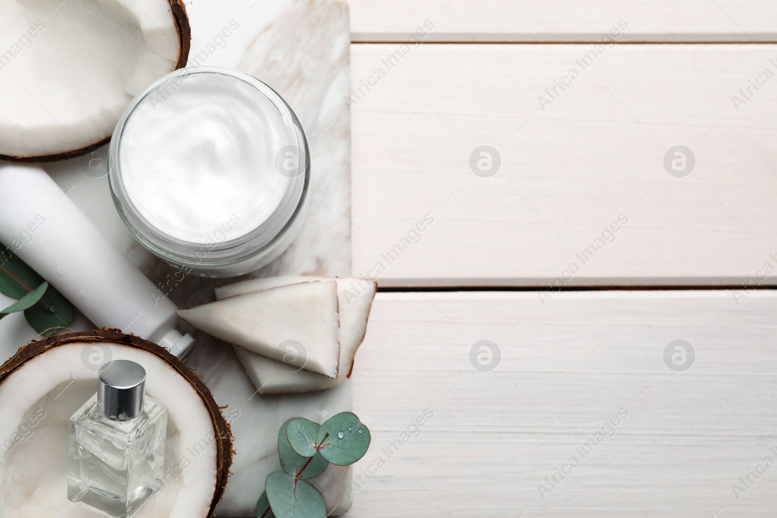 Photo of Different hand care cosmetic products, coconut pieces and eucalyptus branches on white wooden table, top view. Space for text