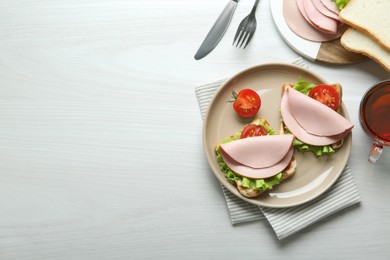 Photo of Plate of tasty sandwiches with boiled sausage, tomato and lettuce on white wooden table, flat lay. Space for text