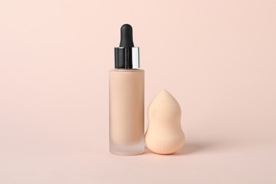 Photo of Bottle of skin foundation and sponge on beige background. Makeup product