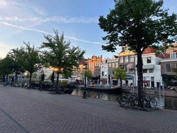 Photo of Leiden, Netherlands - August 1, 2022: Picturesque view of city street with trees and beautiful buildings along canal