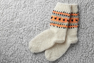 Photo of Knitted socks on grey fur background, flat lay. Space for text