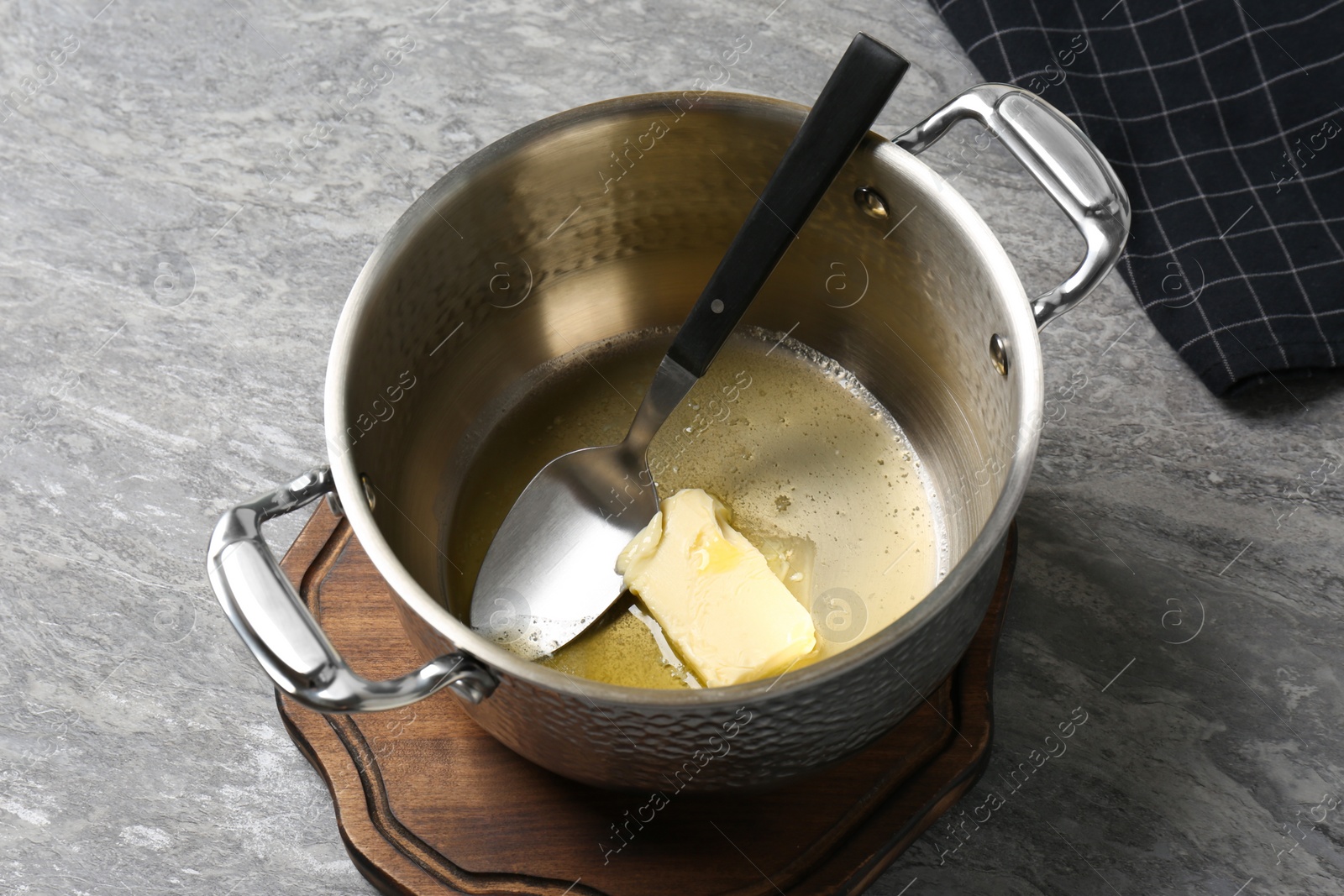 Photo of Pot with melting butter and spoon on grey table