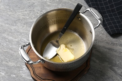 Photo of Pot with melting butter and spoon on grey table