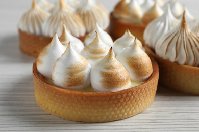 Photo of Many different tartlets with meringue on white wooden table, closeup. Tasty dessert