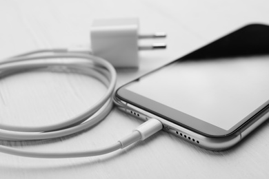 Smartphone and USB charger on white wooden table, closeup. Modern technology