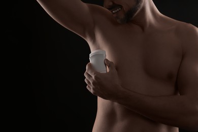 Man applying deodorant on black background, closeup. Space for text