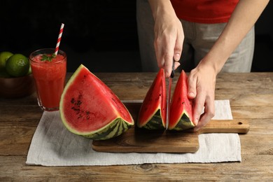 Photo of Woman cutting delicious watermelon at wooden table against dark background, closeup