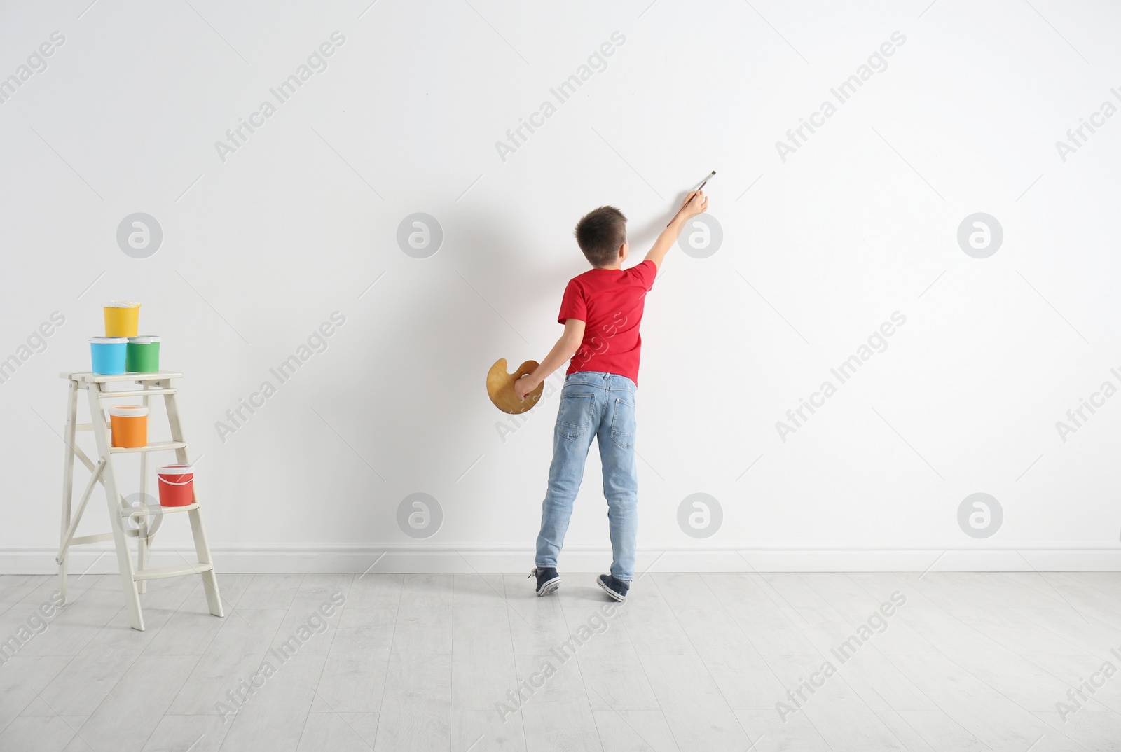 Photo of Little child painting on blank white wall indoors