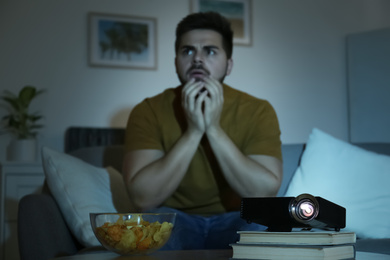 Photo of Young man watching movie at home, focus on video projector