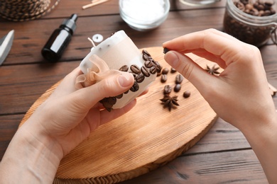 Photo of Woman decorating handmade candle with coffee beans at wooden table, closeup