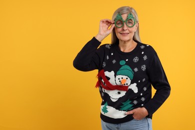 Photo of Happy senior woman in Christmas sweater and funny glasses on orange background. Space for text